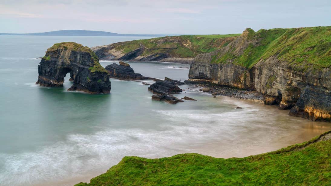 Calm waters and grass covered cliffs at Ballybunion in Co. Kerry.