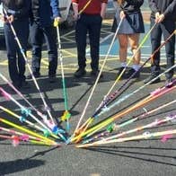 View of lower half of teenagers all holding long, thin, decorated poles into a central point on a playground.