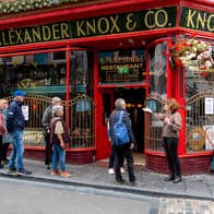 A group of people gather outside a bright red pub on a narrow city street