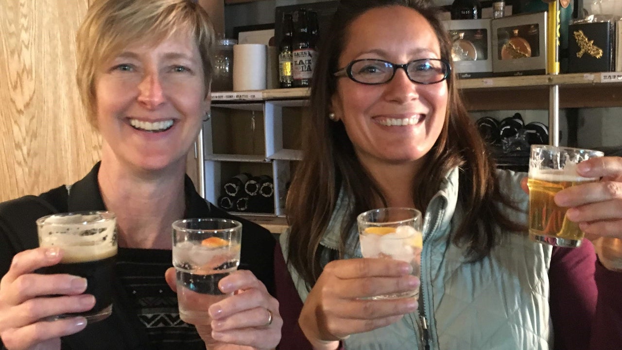 Two people holding a glass in each hand in a beer tasting room