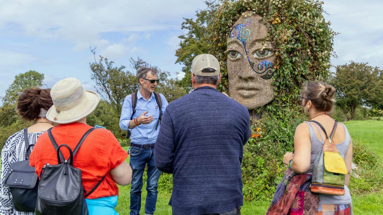 People and a tour guide in a field at a stone monument