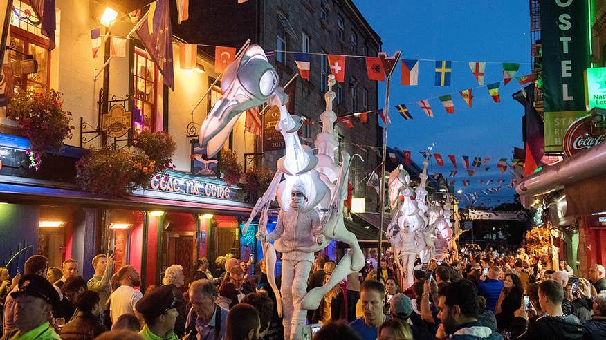 Crowds of people watching a street parade during during the Galway International Arts Festival