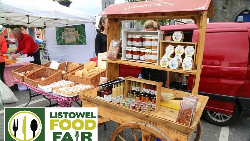 Listowel Food Fair 2025 - A wooden cart holding displays of various potted sauces beside table with wicker baskets containing different baked goods and loaves of bread.