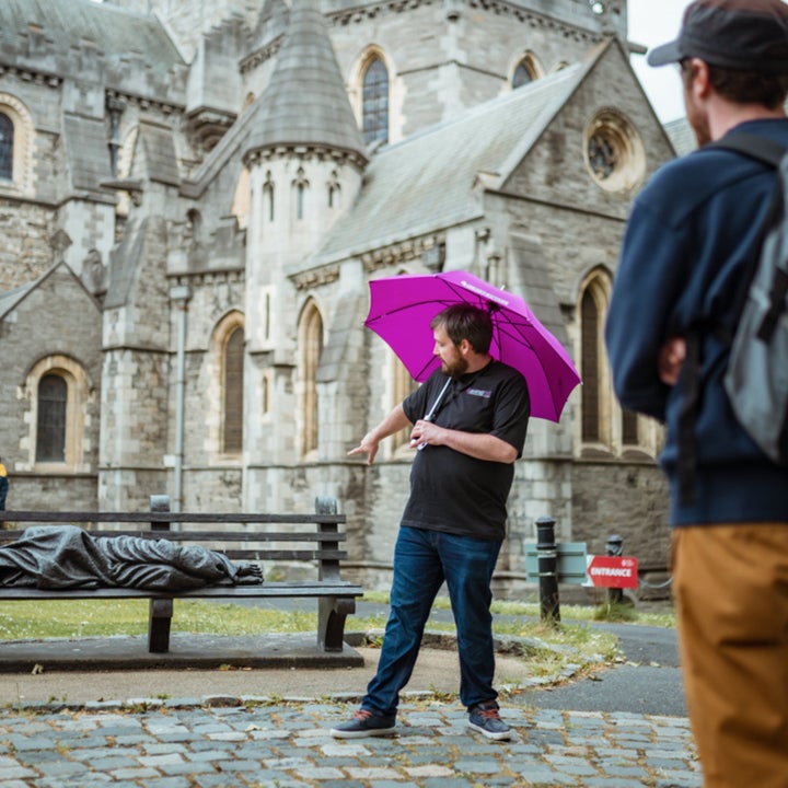 A tour guide giving a tour while pointing at a sculpture on a bench