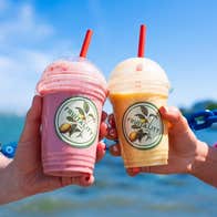 A close up of two people holding plastic cups with straws and colourful liquids