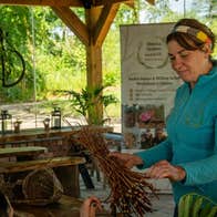 A lady holding a bunch of willow twigs in a workshop with views of trees from the windows