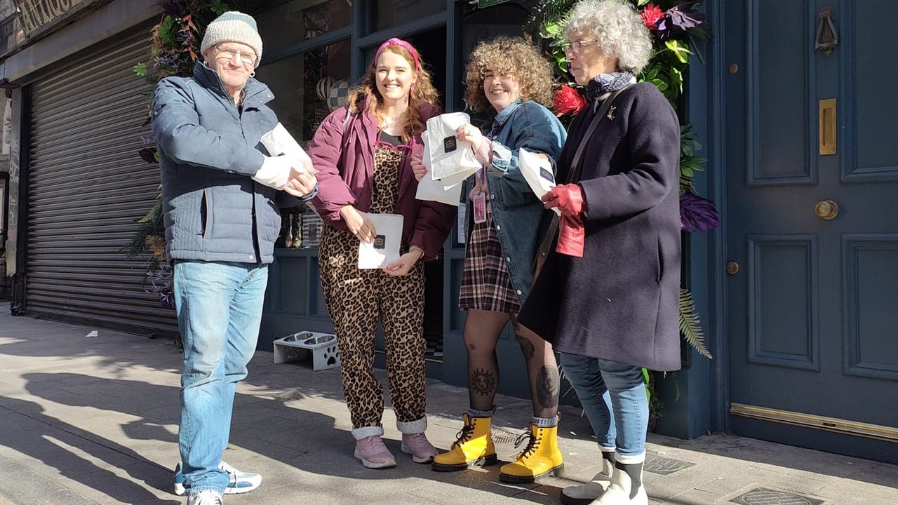 Four people standing outside a pub posing with small branded bags with food on them