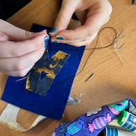 Someone is a creating an artwork by sewing a piece of fabric onto something.