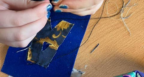 Someone is a creating an artwork by sewing a piece of fabric onto something.