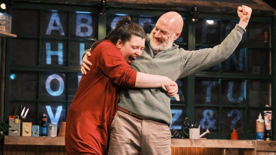 A laughing woman has her arms around an older, happy man who is holding up one arm in a fist