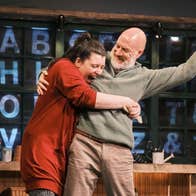 A laughing woman has her arms around an older, happy man who is holding up one arm in a fist