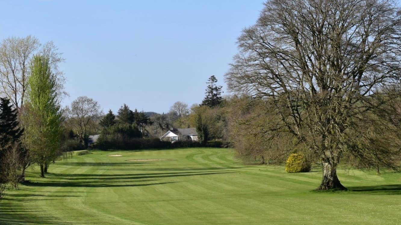 Golf green with trees on either side and a white house in the background