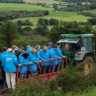 A tour group standing on trailer with a tractor as they enjoy a West Cork Farm Tour.