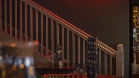 Stairs next to wooden tables and a red neon sign saying bar and restaurant with an arrow pointing upstairs