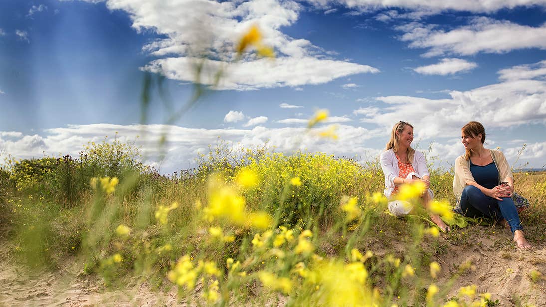 Two friends sitting beside flowers on Malahide Beach, Dublin