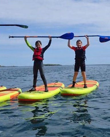 Eight children standing on paddleboards with their paddles held high over their heads