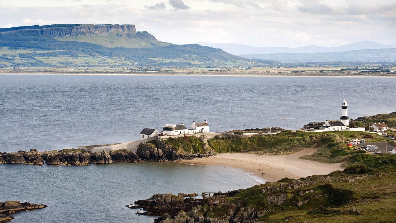 A horse shoe shaped beach with a lighthouse overlooking it