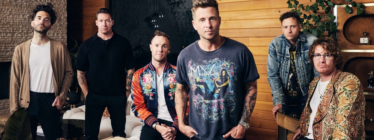 A group of 6 men standing or seated in a scattered group in a room