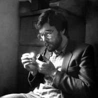 Black and white image of a seated man lighting a pipe.