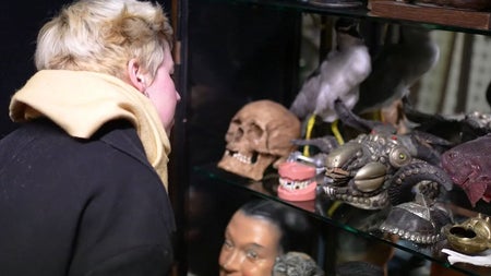 Visitor looking at a cabinet of curiosities including masks and false teeth