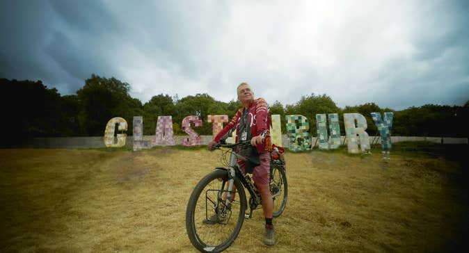 A man on a bicycle in front of letters that spell "Glastonbury".