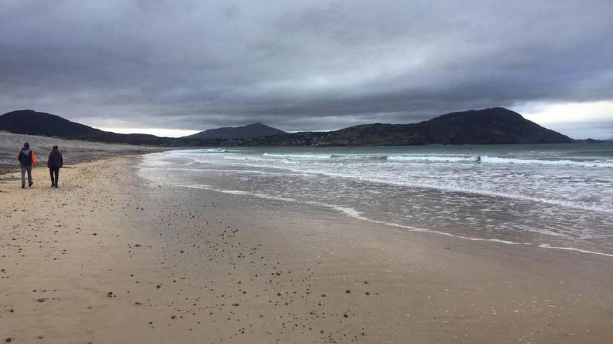 Two people walking along the beach with mountain views in the distance at Pollan Bay, Donegal