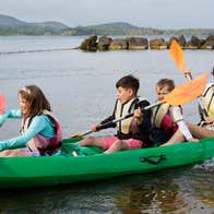 Three children and an adult kayaking on a lake