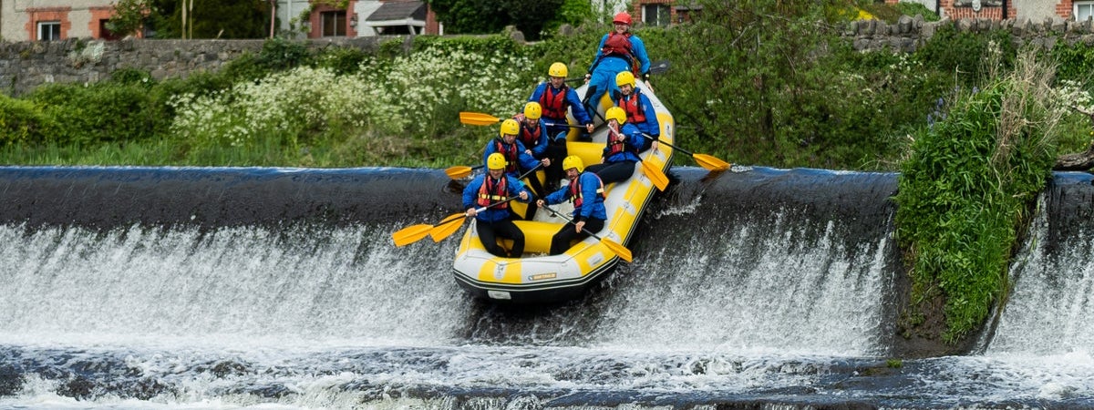 Eight people enjoying themselves rafting over a weir in a single raft