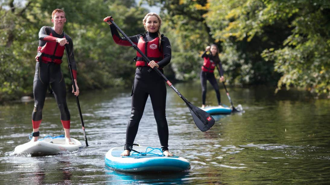 Three people stand-up paddle boarding across a waterway.