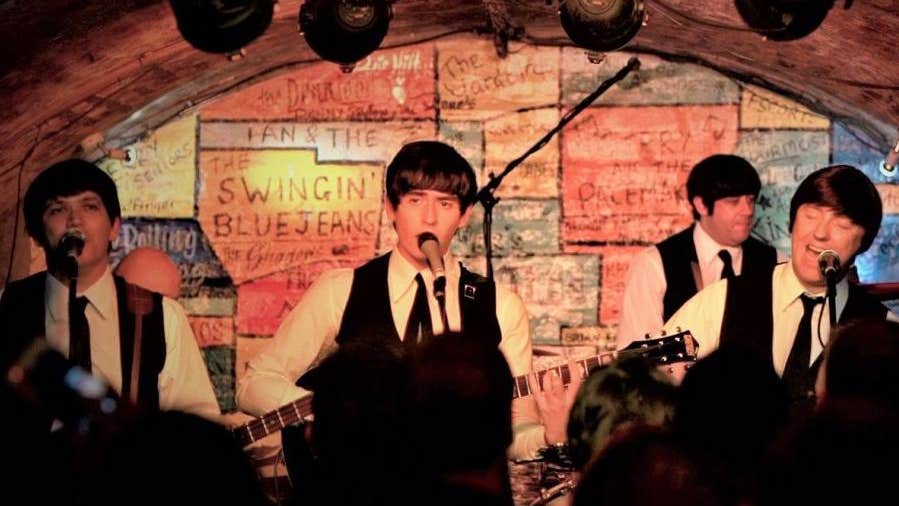 4 men singing and playing on a small stage with low ceiling.