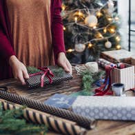A person wrapping a present surrounded by wrapping paper and decorations