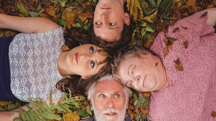 Looking down on 2 couples lying on ground covered in leaves with their heads all touching in a square shape
