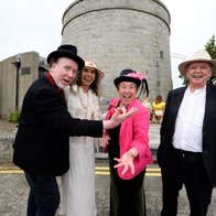 4 people in smart clothes standing in front of a round tower.