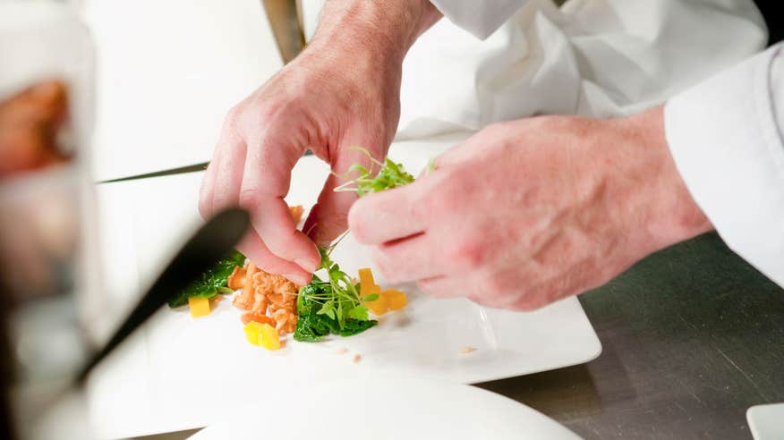 Chef plating food on a square, white, plate
