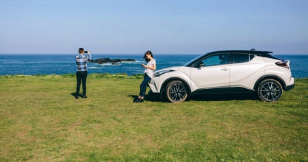 Two people at a scenic coastal location with their hire car