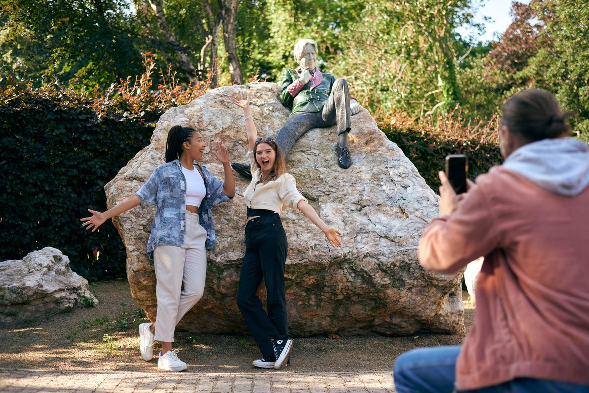 Two friends posing for a picture with the Oscar Wilde statue in Merrion Square while another friend takes the picture.