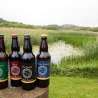 Four bottles of beer with branded labels with a lake view in the background