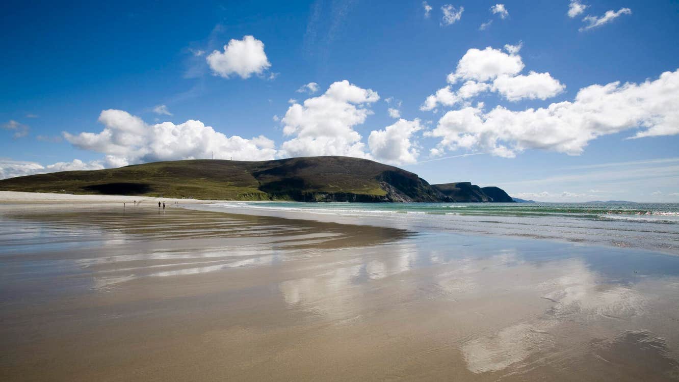 Keel Beach, Achill Island with blue sky, fluffy clouds, and reflections on wet sand