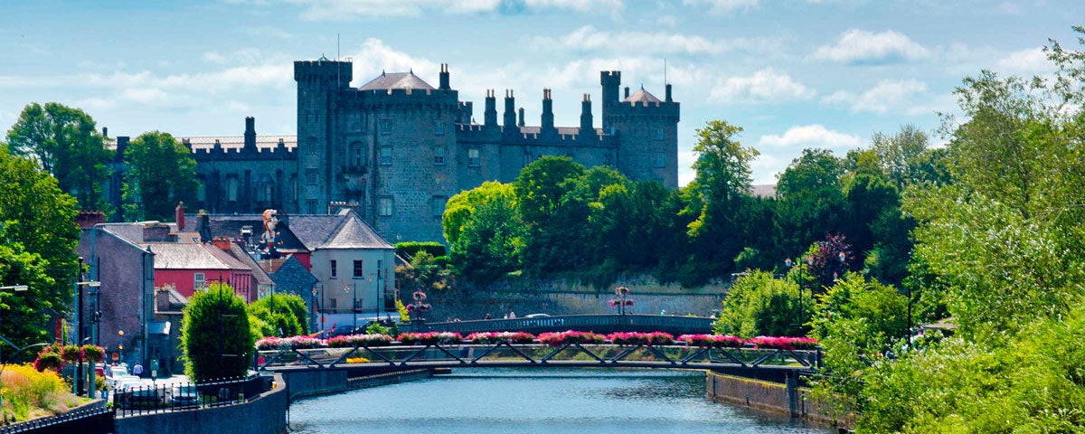 Kilkenny Castle with the River Nore and a pedestrian bridge with flowers