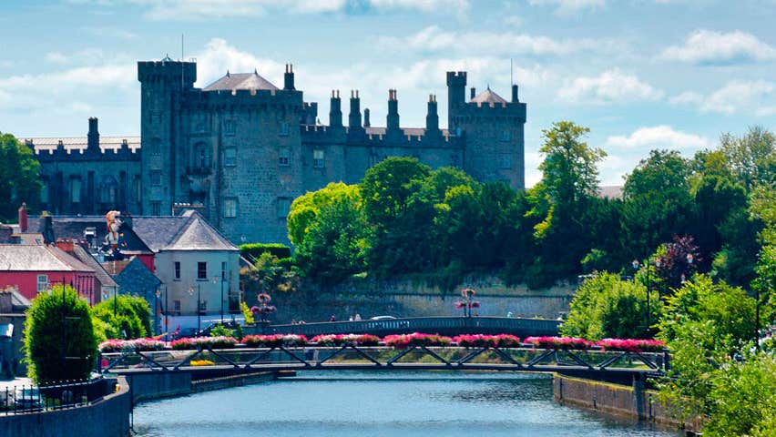 Kilkenny Castle with the River Nore and a pedestrian bridge with flowers