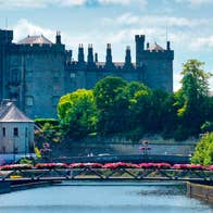Kilkenny Castle with the River Nore and a pedestrian bridge with flowers