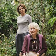 Meredith sits in a rattan chair in the garden, while her daughter Noelle stands behind her.