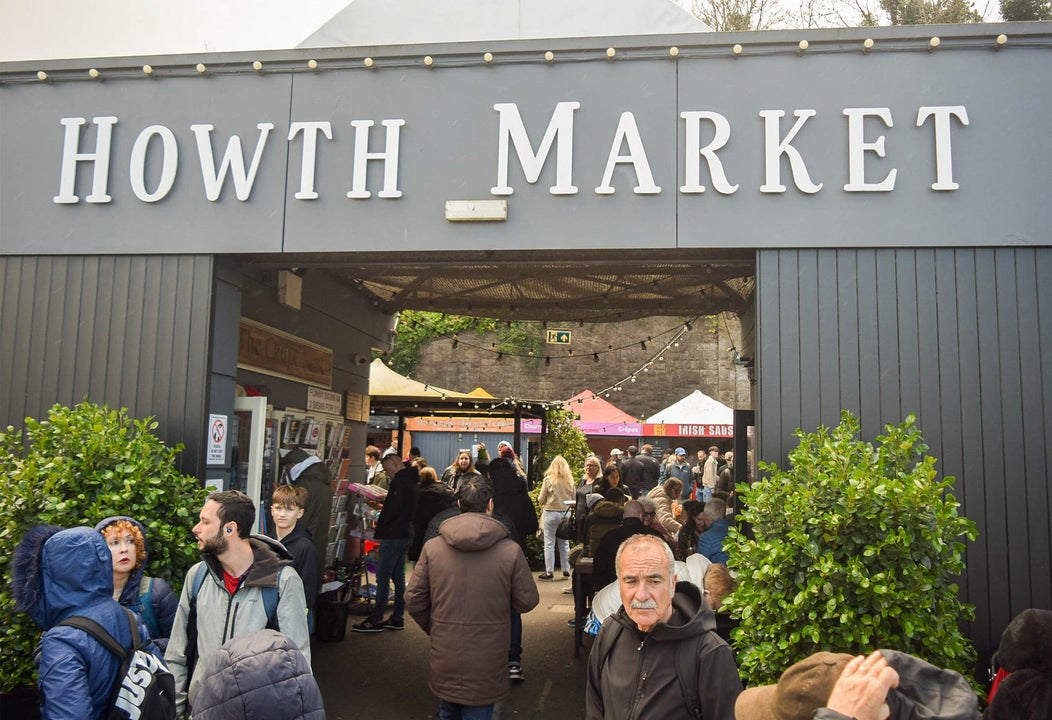 Grey open entrance to a market with a tree either side and people walking through