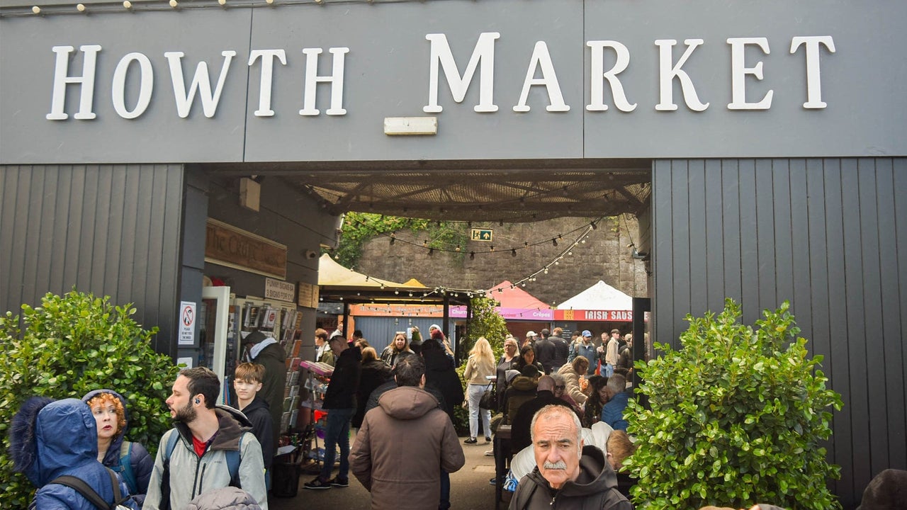 Grey open entrance to a market with a tree either side and people walking through