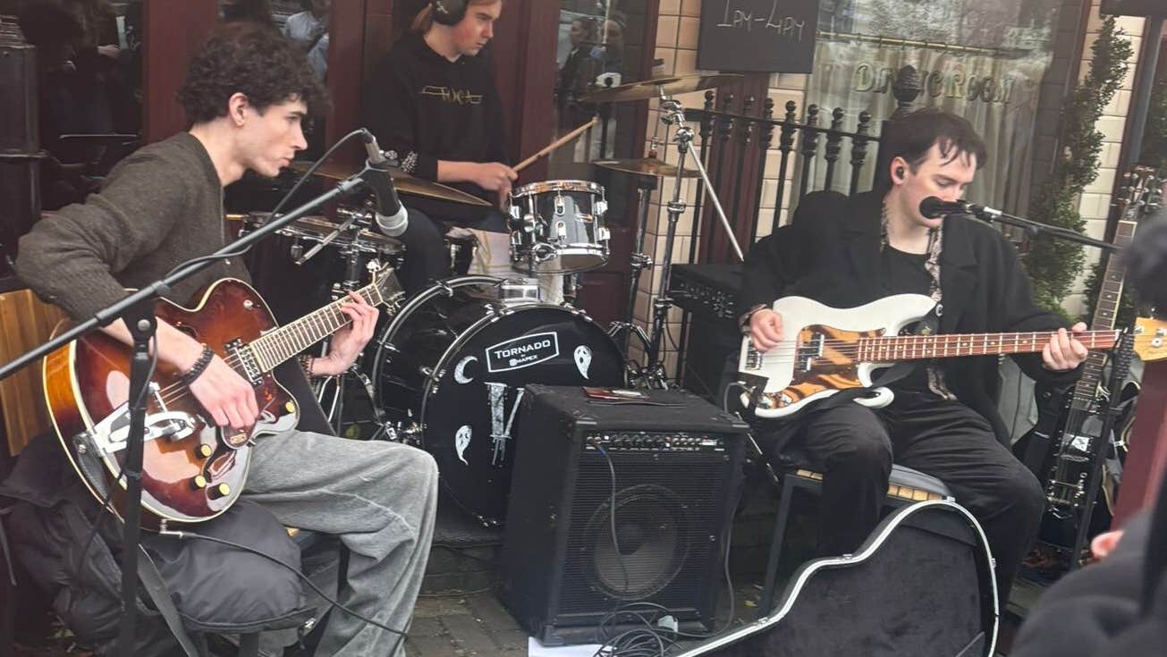 A band of musicians seated, playing outside a shop front.