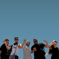 Looking up at a line of 7 happy people, some waving their arms, against a clear blue sky.