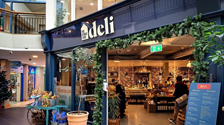 The exterior facade of The Stable Yard Deli painted a dark navy blue with green plants around the entrance.