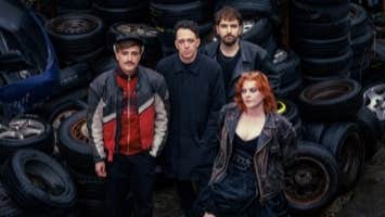 Group of 4 people standing close together surrounded by piles of old tyres and wheels