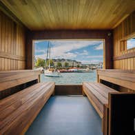 Wood lined sauna interior with bench seating overlooking a harbour through a large open window