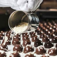 A row of chocolate sweets being sprinkled with flakes during manufacturing